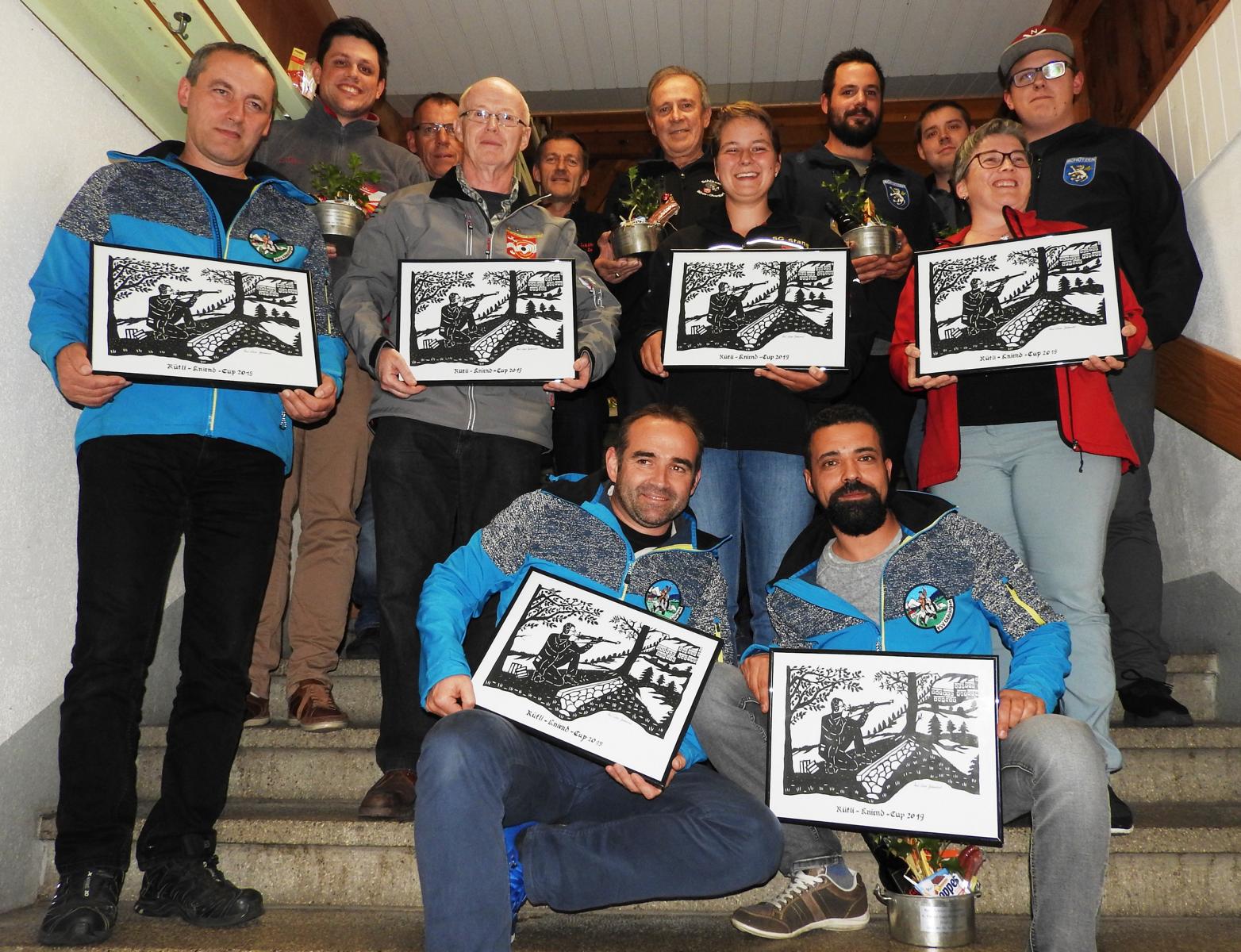 Die 16 Gewinner aus den beiden Kategorien «mit» bzw. «ohne Becher» mit je drei der Rütlischütz-Scherenschnitten: Stehend (v.l.): Beat Odermatt, Erich May, Erika Keiser, Michaela Aschwanden; kniend links Bruno Mathis, rechts Miguel Pinto. In der hintersten Reihe zu erkennen sind die weiteren Gewinner Roberto May, Franz Müller, Hans-Peter Bucher, Dölf Lussi, Stefan Durrer, Luca Amstad und Samuel Christen